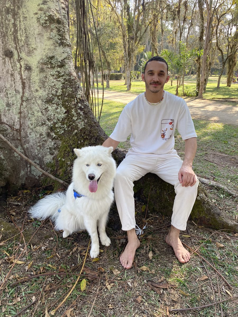 Gaspar sentado em um parque, ao lado de um cachorro branco