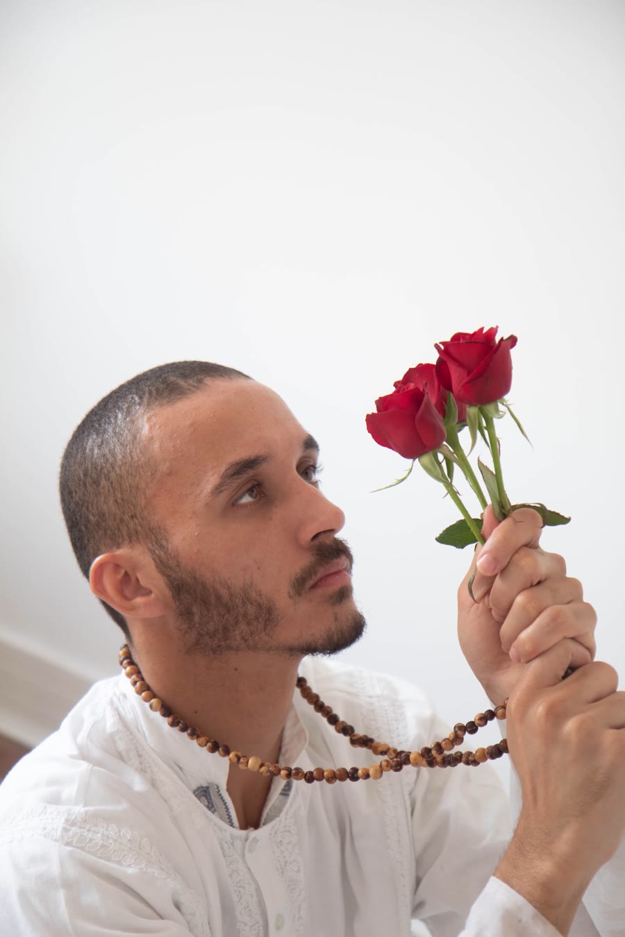 Gaspar de camisa branca e colar de contas, olhando para um buquê de rosas vermelhas
