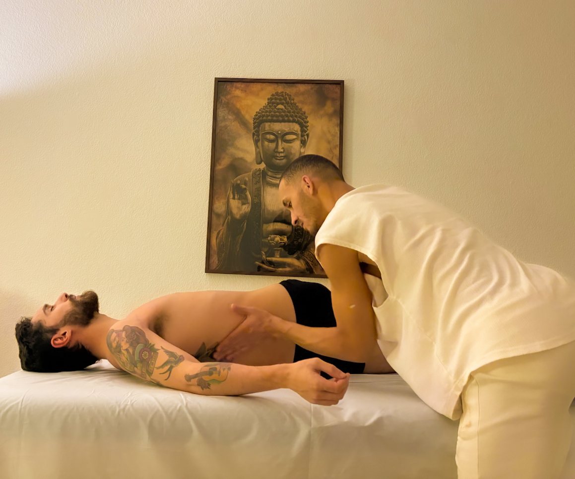Gaspar inclinado sobre a maca, fazendo massagem no braço e na lateral do corpo de um cliente deitado